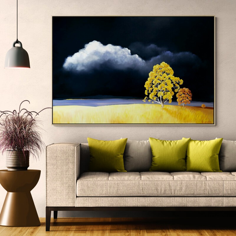 Golden Defiance by Lucinda Leveille displayed in a contemporary interior, original Australian landscape painting featuring dramatic storm clouds, golden grasses and a luminous yellow tree.