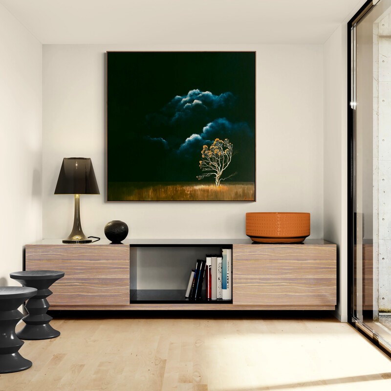 Held by the Light by Lucinda Leveille displayed in an interior setting, original Australian landscape painting featuring a glowing flowering tree beneath dramatic storm clouds and a dark atmospheric sky.